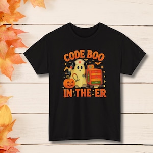 May include: A black short-sleeve t-shirt featuring a graphic of a ghost wearing a nurse cap, holding a syringe, standing next to a pumpkin and a medical cart. The text reads CODE BOO IN THE ER in orange letters, surrounded by small stars and bats.