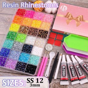 May include: A clear plastic organizer box filled with multi-colored resin rhinestones in SS 12 3mm size, accompanied by a pink gift box, four green and purple trays, two pink pens, a white scoop, a black tool, a white pencil, and four B-7000 glue tubes.
