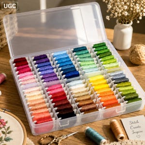 May include: A clear plastic storage box containing a large collection of embroidery floss wound onto white cardboard bobbins. The threads are organized by color in individual compartments, featuring a full spectrum of shades including red, blue, green, yellow, and pink.