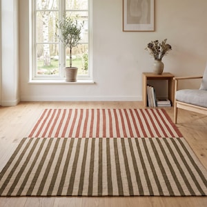May include: A rectangular area rug featuring a two-tone striped pattern. The top half of the rug displays vertical stripes in terracotta and cream, while the bottom half features vertical stripes in olive green and cream, creating a distinct color block.