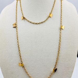 Pode incluir: Um colar dourado com um design de corrente delicado. O colar apresenta pequenos pingentes de borboleta espaçados uniformemente ao longo da corrente. O colar é exibido em um manequim.