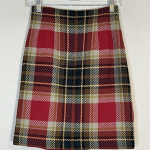 May include: A plaid skirt in shades of red, brown, green, and yellow. The skirt is a classic A-line shape, with a high waist and a hem that falls just above the knee. The fabric has a woven texture.