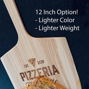 May include: A wooden pizza peel with a handle, featuring the text "PIZZERIA" and "EST. 2020". The peel is light-colored and has the text "12 Inch Option! - Lighter Color - Lighter Weight". A pizza is partially visible on the peel.
