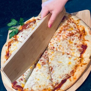 May include: A freshly baked pizza with melted cheese and tomato sauce, sliced and served on a wooden pizza peel. The pizza is being cut with a wooden pizza cutter. A sprig of parsley adds a fresh touch.