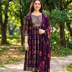 May include: A deep purple knee-length dress featuring a geometric and circular print, a notched neckline with metallic embroidery, three-quarter sleeves, and a matching purple dupatta with a tie-dye pattern, paired with solid purple leggings.