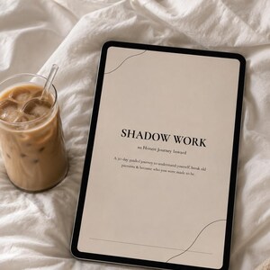 Pode incluir: Um tablet exibindo um documento digital bege intitulado SHADOW WORK an Honest Journey Inward, com uma descrição de jornada guiada de 30 dias, gráficos de linhas pretas finas e um copo de café gelado com canudo ao lado do dispositivo.