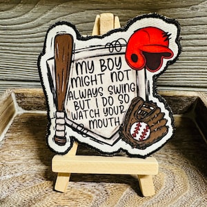 May include: A brown and white baseball themed patch with the text "My boy might not always swing but I do so watch your mouth". The patch features a baseball bat, a baseball glove, and a baseball cap.
