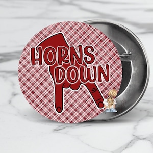 May include: A round button with a red and white plaid pattern. The button features a red hand gesture with the words "HORNS DOWN" in red. The button is made of metal.