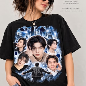Peut inclure: Un t-shirt noir à manches courtes avec une impression graphique de l'artiste Suga de BTS. Le motif comprend plusieurs portraits de l'artiste, le texte "SUGA" en grande police bleue, le logo BTS et le nom "Min Yoongi" en écriture cursive.