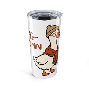 Puede incluir: Un vaso de acero inoxidable blanco con tapa de plástico transparente que presenta una oca de dibujos animados con un gorro beige, gafas naranjas en forma de corazón y una bufanda color óxido. El texto Hello Autumn está en marrón.