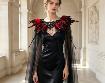 Può includere: Un abito lungo in raso nero con un mantello in tulle nero trasparente. Lo scollo è decorato con un colletto in pizzo nero arricchito da piume rosse e nere e da un ciondolo centrale con pietra rossa e catenelle pendenti.