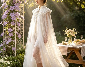 Può includere: Una cappa lunga fino ai piedi in tulle bianco trasparente con colletto alto e un coprispalle decorativo smerlato con ricami complessi. Il tessuto traslucido è decorato con piccole perle bianche sparse su tutto il capo.