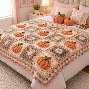 May include: A handmade crochet blanket featuring a repeating pattern of cream, sage green, and dusty pink squares, with several three-dimensional orange pumpkins attached to the surface. The blanket has a scalloped edge and a soft, textured yarn finish.
