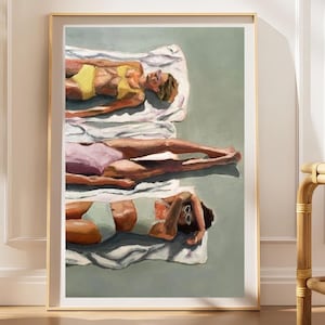 May include: A framed art print depicting three figures lying on white towels on a solid green surface. The top figure wears a yellow bikini, the middle figure wears a lavender swimsuit, and the bottom figure wears a light green bikini.
