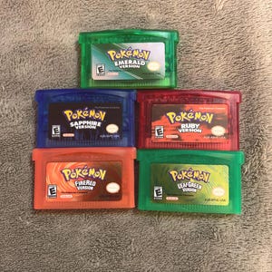May include: Five Nintendo Game Boy Advance video game cartridges including Pokémon Emerald, Sapphire, Ruby, FireRed, and LeafGreen versions. Each rectangular plastic cartridge features a colorful label with the game title and an ESRB E rating.