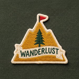 May include: A triangular embroidered patch featuring a mustard yellow mountain shape with a dark green pine tree in the center, a small red flag at the peak, and a white banner across the bottom with the word WANDERLUST in green text.