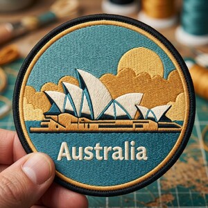 May include: A circular embroidered patch featuring the Sydney Opera House in white with blue accents against a teal background. A golden sun and clouds are visible above the structure. The word Australia is stitched in white at the bottom.