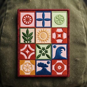 May include: A rectangular embroidered patch featuring a grid of twelve squares, each displaying a unique icon including a red wheel, blue cross, green flower, green leaves, yellow sun, red geometric shape, blue wave, and a dark blue mountain.