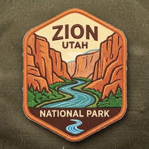 May include: A hexagonal embroidered patch featuring a landscape of Zion National Park in Utah. The design shows orange canyon walls, a winding blue river, and green trees. The text ZION UTAH is at the top and NATIONAL PARK is at the bottom.