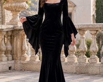 May include: A floor-length black velvet dress featuring a square neckline, long fitted sleeves that flare into wide, dramatic bell-shaped cuffs, and a form-fitting bodice that transitions into a flared mermaid-style skirt that pools at the floor.