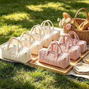 Puede incluir: Una colección de bolsos rectangulares de pana con un patrón de corazones acolchados y asas superiores. Los bolsos están disponibles en crema y rosa empolvado, cada uno con nombres bordados como Grace, Mia, Zara y Author en la parte frontal.