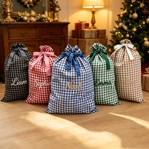 Puede incluir: Cinco bolsas de regalo de tela con cordón y estampado de cuadros vichy en negro, rojo, azul, verde y marrón. Cada bolsa está atada con una cinta a juego y bordada con un nombre: Liam, Sophia, Noah, Emma y Mia en letras doradas cursivas.