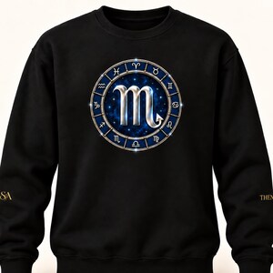 May include: A black long-sleeve sweatshirt featuring a central circular graphic of the Scorpio zodiac symbol in silver. The symbol is surrounded by a blue ring containing all twelve zodiac signs against a starry, deep blue nebula background.