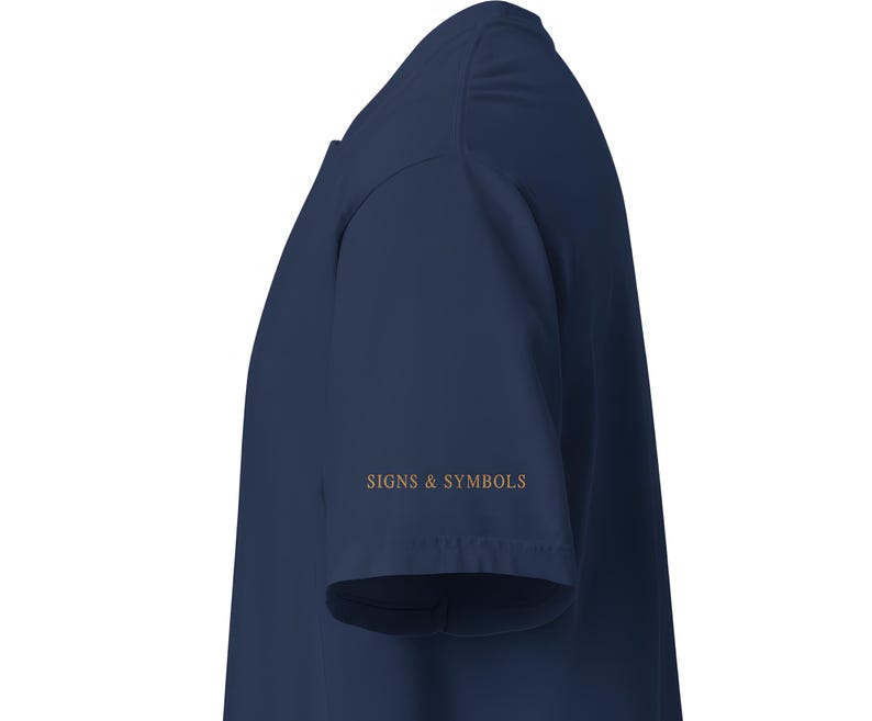 May include: A dark navy blue short-sleeved t-shirt viewed from the side. The sleeve features the text SIGNS & SYMBOLS printed in a metallic gold font. The garment has a simple, clean construction with a standard hemline on the sleeve and body.
