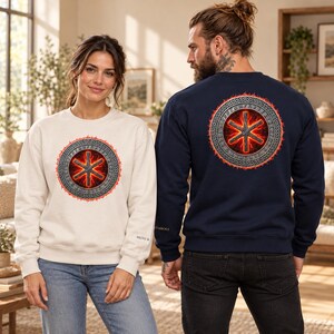 May include: A cream-coloured crewneck sweatshirt and a navy blue crewneck sweatshirt, both featuring a circular graphic on the chest and back. The design displays a glowing red six-pointed star symbol enclosed within a silver Celtic knot border.