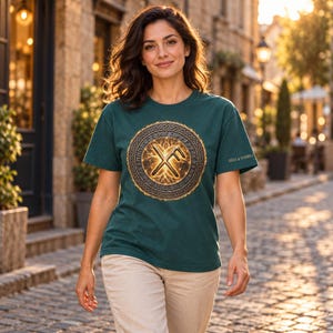 May include: A dark teal short-sleeve t-shirt featuring a circular graphic on the chest. The design includes a central golden rune symbol surrounded by a detailed knotwork border and an outer ring of runic characters. The text SIGNS & SYMBOLS is printed on the sleeve.