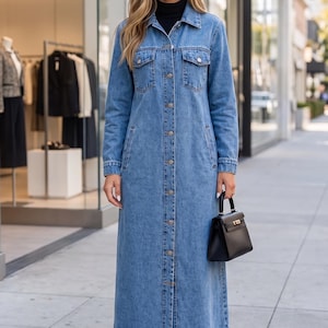 Peut inclure: Une robe chemise longue en jean bleu, arrivant jusqu'aux pieds, dotée d'un col classique, d'une fermeture boutonnée sur toute la longueur et de deux poches poitrine à rabat boutonné. Elle est portée sur un haut noir à col montant et un sac à main.