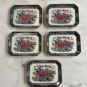 May include: Five rectangular ceramic dishes featuring a cream-colored center with a floral design of red peonies and blue branches. The borders are decorated with a dark blue and white geometric pattern, finished with a thin orange-brown rim.