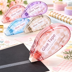 Puede incluir: Cinco dispensadores de cinta adhesiva de plástico translúcido en colores rosa, morado, azul y transparente. Cada dispensador tiene una etiqueta blanca con el texto Glue Tape, Strong & Long Lasting y Scrapbook con un pequeño icono de corazón.