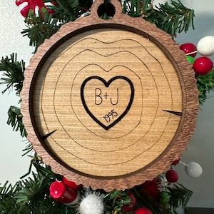 May include: A wooden Christmas ornament shaped like a tree trunk with a heart carved into it. The heart has the initials "B+J" and the year "1995" inside.