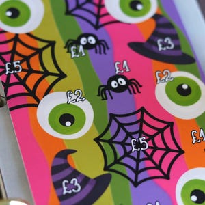May include: A rectangular planner insert featuring a colourful Halloween pattern with green eyeballs, black spiderwebs, spiders, and purple witch hats. Each icon is labelled with currency values including £1, £2, £3, and £5, printed on a striped background.