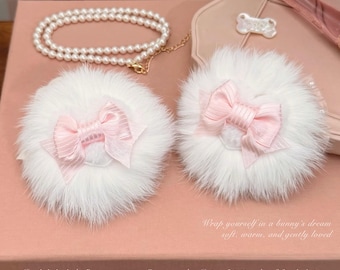 May include: Two round white faux fur hair accessories featuring light pink ribbon bows, accompanied by a white pearl necklace. The text on the surface reads: Wrap yourself in a bunny's dream soft, warm, and gently loved. Just little lamb | BUNNY-CODED LOVERS COLLECTION | Dairy of puppy | Softie Aesthetic.