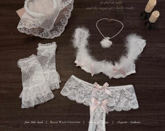 May include: A white lace lingerie set including a bra with feather trim and pink bows, matching lace panties, fingerless gloves, a lace headpiece, and a pearl necklace. Text reads: Dance like a coquette - draped in tulle and the magic of a ballet waltz.