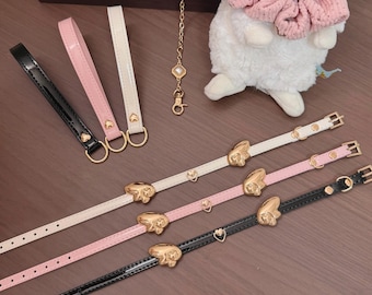 May include: Three glossy faux leather straps in black, pink, and white, each featuring gold-tone heart-shaped charms and buckles. Included are three matching wristlet loops with heart accents, a gold chain with a charm, and a plush white rabbit toy.