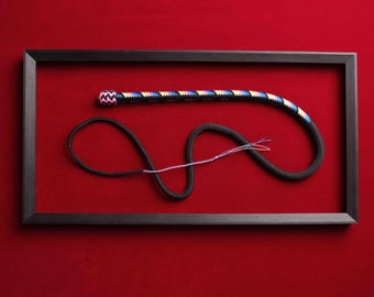 May include: A black braided whip featuring a handle with a vibrant multi-colored chevron pattern in pink, blue, and yellow. The whip includes a long black cord section that terminates in a thin, frayed multi-colored fiber tail end.