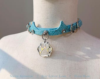 May include: A light blue textured choker collar featuring a crown-shaped top edge, silver-toned metal hardware, and a dangling paw print charm. The text "Softie Aesthetic | Just Little Lamb | Hand Made" is visible at the bottom of the image.