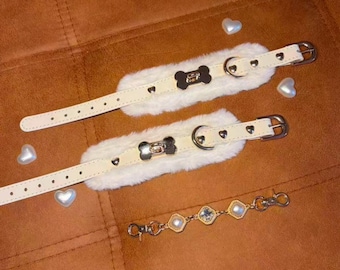 May include: Two cream-colored collars with white faux fur lining, silver-tone heart-shaped studs, and bone-shaped metal accents. A separate silver-tone chain features four square links with embedded white faux pearls and lobster clasps.