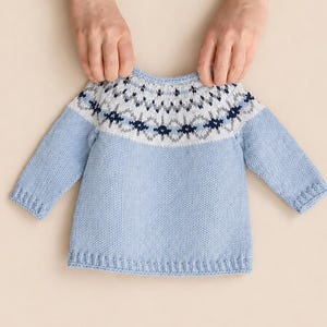 Può includere: Un maglione a maniche lunghe color azzurro con scollo rotondo e uno sprone bianco decorato con un motivo geometrico nei toni del blu scuro e del grigio. Il capo è realizzato con colletto, polsini e orlo in maglia a coste.