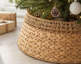 Könnte beinhalten: Ein runder, konischer Weihnachtsbaumständer aus geflochtenem, natürlichem Seegras. Die Basis weist ein dichtes Flechtmuster auf, während der obere Bereich ein dekoratives, offenes Gitterdesign in einem passenden hellen Beigeton zeigt.