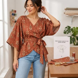Könnte beinhalten: Ein rostfarbenes Wickeloberteil mit Kimonoärmeln und Taillenband, verziert mit einem sich wiederholenden botanischen Muster in Creme und Salbeigrün. Ein weißes Schild zeigt den Text WRAP KIMONO-SLEEVE TIE TOP SEWING PATTERN mit einer Strichzeichnung.