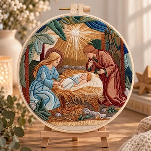 May include: A circular embroidery hoop featuring a nativity scene with a figure in a blue robe and a figure in a red robe kneeling beside a baby in a manger. A bright sunburst is stitched above the figures, surrounded by green foliage.