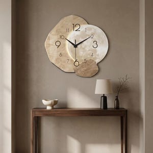 May include: A wall clock with an irregular, layered design featuring a beige, marble-like texture. The clock face displays black Arabic numerals and thin black hands. A circular, illuminated moon-like graphic is centered behind the clock hands.