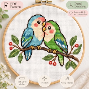 May include: A cross-stitch pattern in a wooden hoop featuring two lovebirds, one blue and one green, perched on a brown branch with green leaves and red berries. Text includes PDF Pattern, Digital Download, Pattern Only, 184 x 148 stitches, 17 colors.