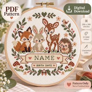May include: A cross-stitch pattern in a wooden hoop featuring a fox, rabbit, fawn, and hedgehog surrounded by a floral wreath. The design includes a banner for a name and birth date, with text indicating 200 x 200 stitches and 22 DMC colors.