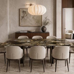 Puede incluir: Una mesa de comedor rectangular con una superficie de piedra ágata pulida de color marrón oscuro y una base robusta, rodeada por ocho sillas tapizadas de color crema con patas de madera oscura, en una estancia con lámpara y aparador.