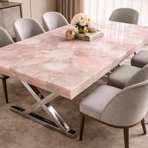 Peut inclure: Une table à manger rectangulaire avec un plateau en dalle de quartz rose poli et une base en métal argenté en forme de X, entourée de six chaises rembourrées gris clair avec des pieds en bois foncé, avec un centre de table floral.